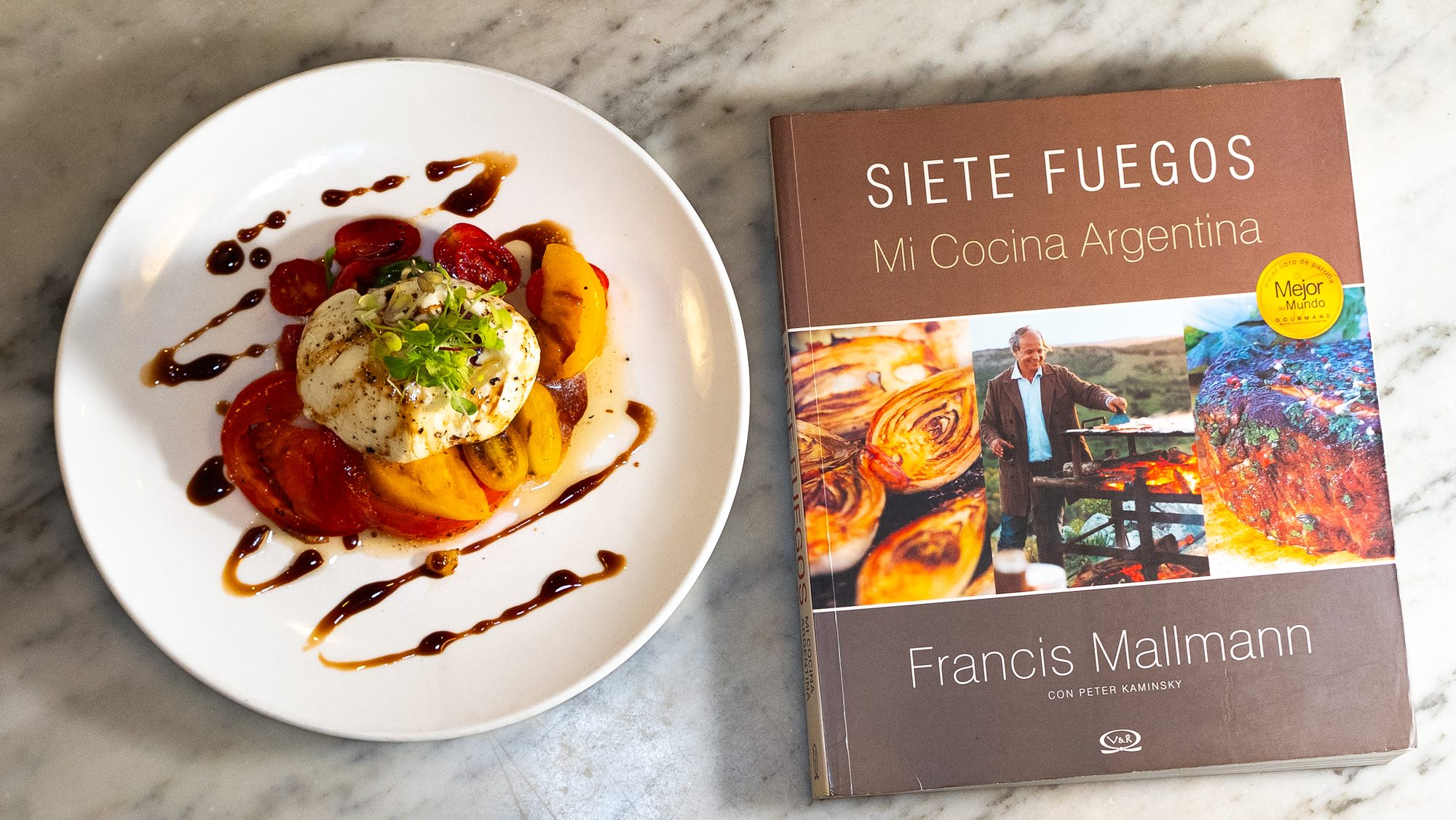 Burrata con tomates heirloom junto al libro de cocina Siete Fuegos de Francis Mallmann