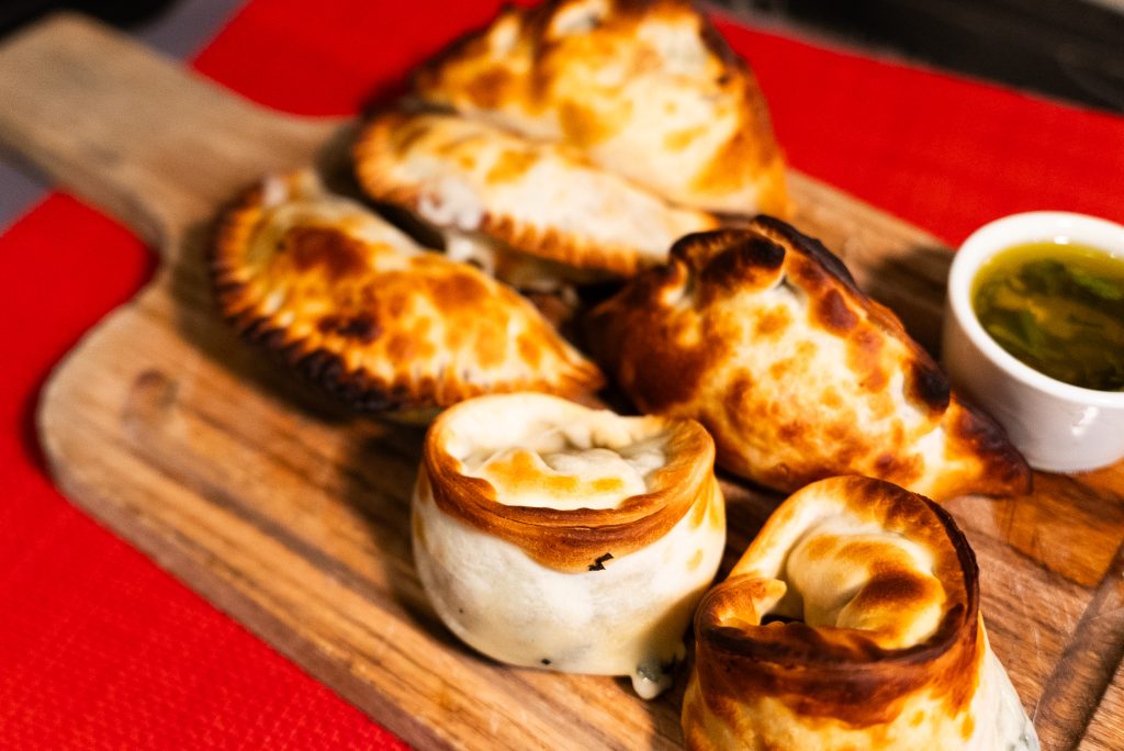 Freshly baked Argentine empanadas with golden crust served on a wooden board.
TITLE: Authentic Argentine Empanadas Fresh from the Oven
